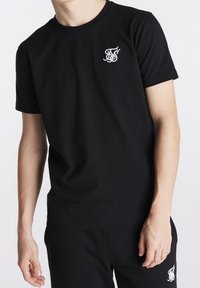 Zwarte katoenen t-shirt met ronde hals, voorzien van een klein wit geborduurd logo op de linkerborst, korte mouwen en een standaard pasvorm.