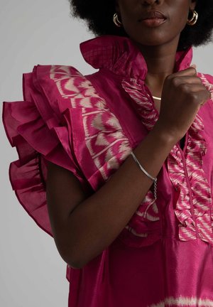 Fuchsia silkeskjorta med volangärmar och mönstrad detaljering, med hög krage och en dekorativ, texturerad design. Silverarmband som accent.