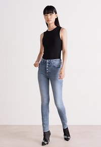 Blå skinny jeans med hög midja, femknapsstängning och en slät denimtextur, tillsammans med en svart ärmlös topp och svarta klackar.