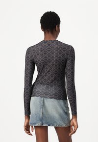 Long-sleeve top in black with a geometric grey pattern, made from a smooth, lightweight material. Paired with a denim skirt.
