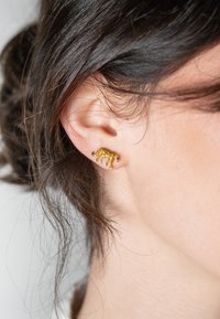 Orecchino a forma di leopardo color oro con accenti neri, posizionato su un orecchio. I dettagli intricati evidenziano le caratteristiche e la texture dell'animale.