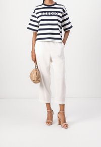 Camisa corta a rayas en navy y blanco con el texto "STUDIO", combinada con pantalones cortos de lino blancos y un bolso beige. Lleva sandalias de tacón cuadrado.