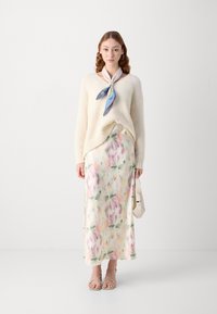 Pull en tricot crémeux et moelleux associé à une jupe maxi à motifs floraux pastel. Tient un sac à main blanc ; porte des sandales légères à lanières.