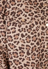 Leopard print fabric with a flap pocket secured by a round gold snap button and matching gold snap buttons along the adjacent seam.
