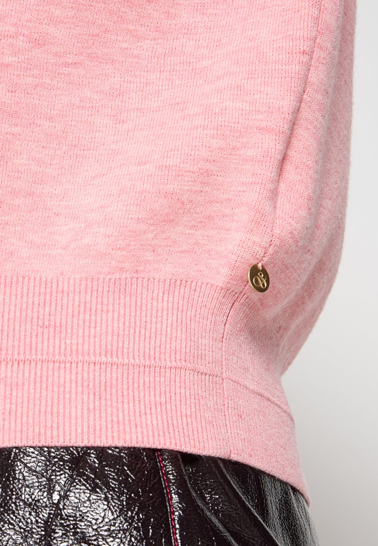 Roze gebreide trui met een ribbelzoom, voorzien van een klein gouden logoaccent aan de zijkant. Zachte textuur met een subtiel gemêleerd patroon.