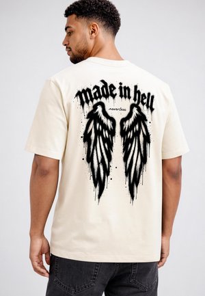Mann trägt ein weißes T-Shirt mit schwarzen Graffiti-Engelsflügeln und dem Text "made in hell nevertheless" auf dem Rücken.