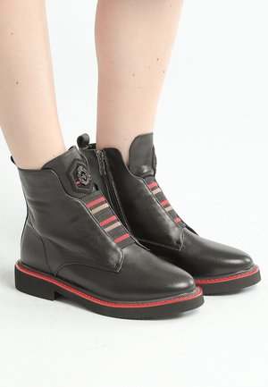 Bottines en cuir noir avec des accents rouges, fermeture éclair sur le côté et panneaux élastiques rayés avec des motifs en chevrons rouges et roses. Semelle durable.
