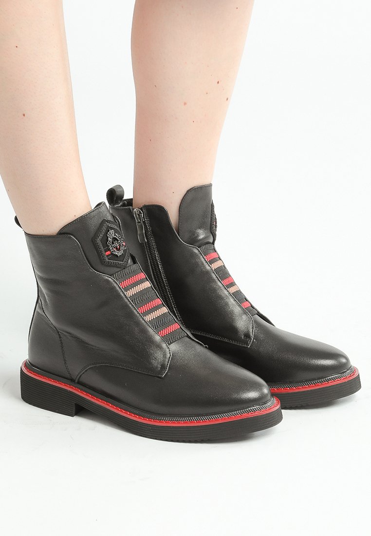 Bottines en cuir noir avec des accents rouges, fermeture éclair sur le côté et panneaux élastiques rayés avec des motifs en chevrons rouges et roses. Semelle durable.
