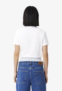 Top bianco a maniche corte con scollatura rotonda, abbinato a jeans blu a vita alta con cintura elasticizzata e una patch in pelle marrone con logo.