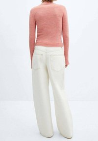 Person wearing a pink long-sleeve sweater and high-waisted wide-leg white pants, standing with their back to the camera.