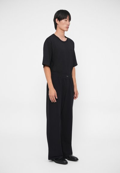 Camiseta negra de manga corta y pantalones sueltos hechos de una tela suave y lisa. El conjunto presenta un diseño simple y minimalista con un corte relajado.