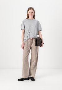Gray oversized t-shirt with side tie, paired with beige wide-leg jeans featuring decorative stitching, and black shoes, held with a dark clutch.