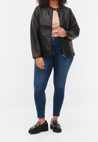 Veste en simili cuir noir avec un col arrondi, fermeture éclair et coupe décontractée, associée à un jean bleu taille haute et des mocassins noirs.