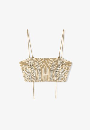 Korte top van beige stof met witte borduursels en zilveren versieringen, voorzien van verstelbare bandjes en een gestructureerde vorm.