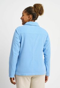 Giacca in corduroy azzurro chiaro con colletto, maniche lunghe e taglio dritto. Presenta dettagli cuciti sul retro e una vestibilità rilassata.