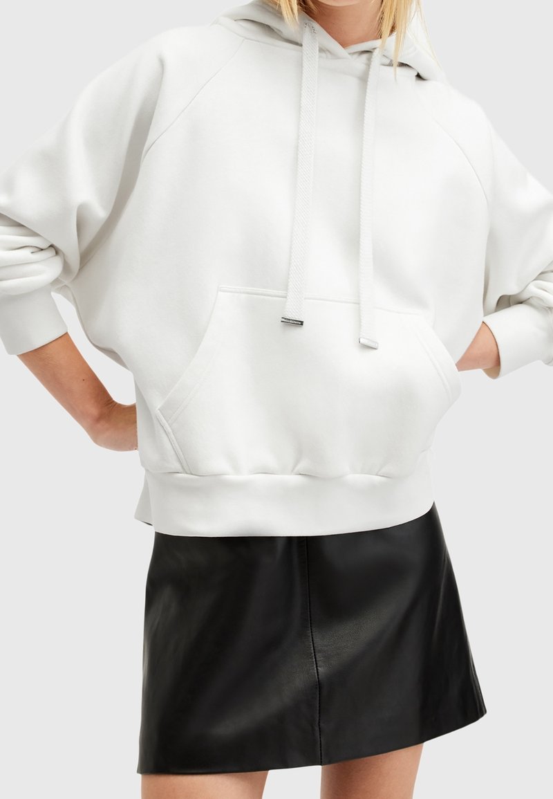 Witte hoodie met een voorzak, verstelbare trekkoorden en geribbelde manchetten, gecombineerd met een zwarte leren minirok. Gladde textuur en ontspannen pasvorm.