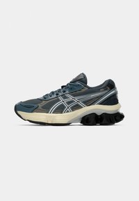 Chaussures de sport avec une tige en mesh texturé gris et bleu, des accents argentés, et une semelle épaisse et rembourrée avec une semelle extérieure en caoutchouc noir ondulé.