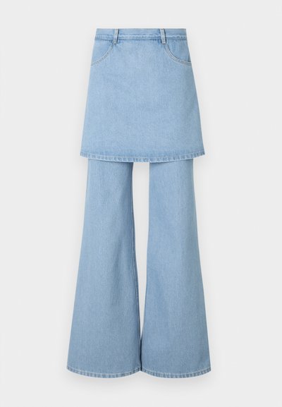 Denimová kombinacija krila in hlač, izdelana iz svetlo modrega materiala, z razširjenimi hlačnicami in vidnimi šivi. Načrtovana je z sprednjimi žepi in pasom.