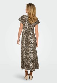 Robe maxi à imprimé léopard avec des manches courtes, fabriquée en tissu doux, elle présente une coupe fluide et une légère taille empire. Chaussures à coins marron.
