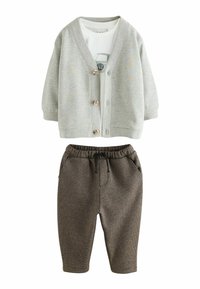 Grijze katoenen cardigan met houten knopen over een witte T-shirt met een autografiek. Bruine gebreide joggers met elastische tailleband en zakken.