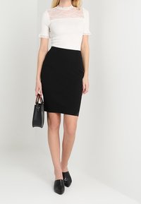 Top blanco con acentos de encaje y mangas cortas, combinado con una falda lápiz negra. Los accesorios incluyen un pequeño bolso negro y zapatos planos negros puntiagudos.