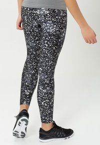 Leggings de estampado de leopardo en negro y gris con un diseño ajustado, fabricados en material elástico, combinados con zapatillas deportivas negras.