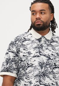 Polo majica s kratkim rukavima u bijeloj boji s crnim printom tropskih palmi, s kontrastnim bijelim ovratnikom i dizajnom kopče s gumbima.