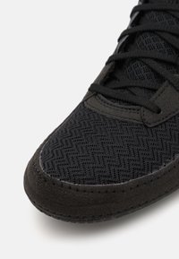 Svart sneakers med en teksturert overdel laget av mesh og semsket skinn, med et sikksakkmønster og flate sorte lisser. Distinkt søm langs kantene.
