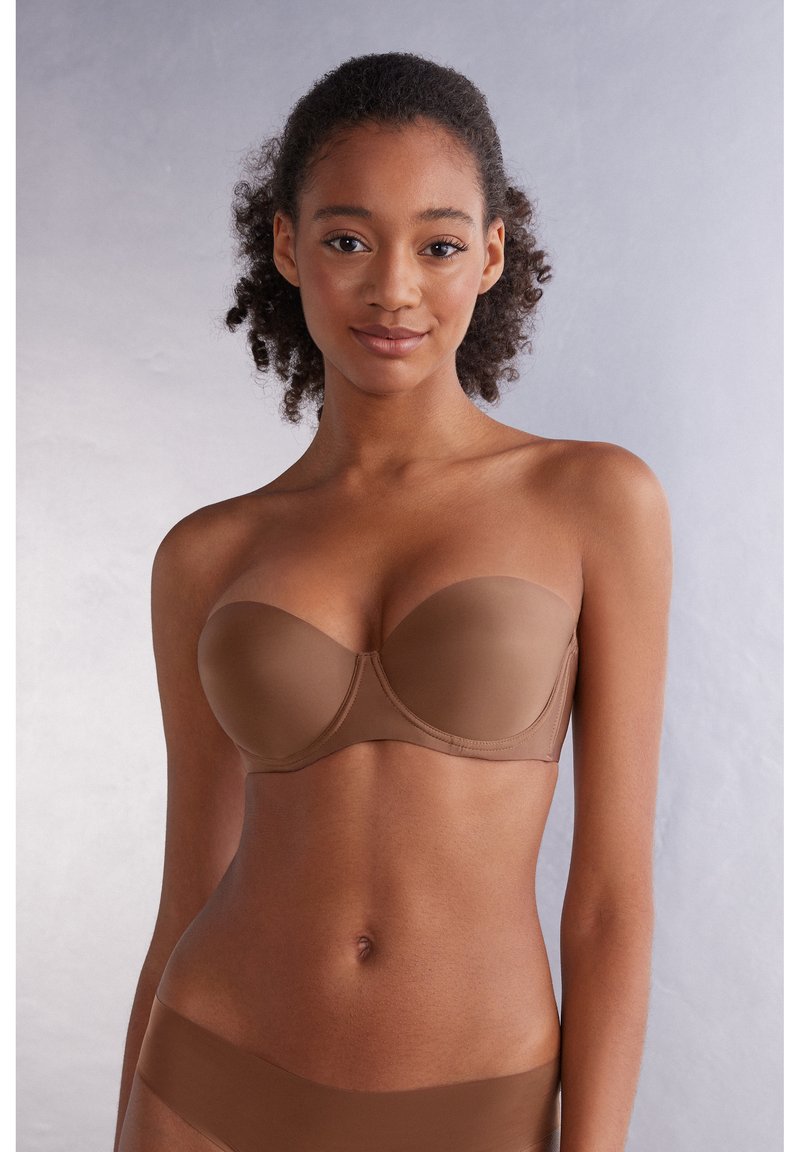 Strapless bh in een middelbruine kleur, naadloze cups, gladde textuur, baleinondersteuning en subtiele stiksels.