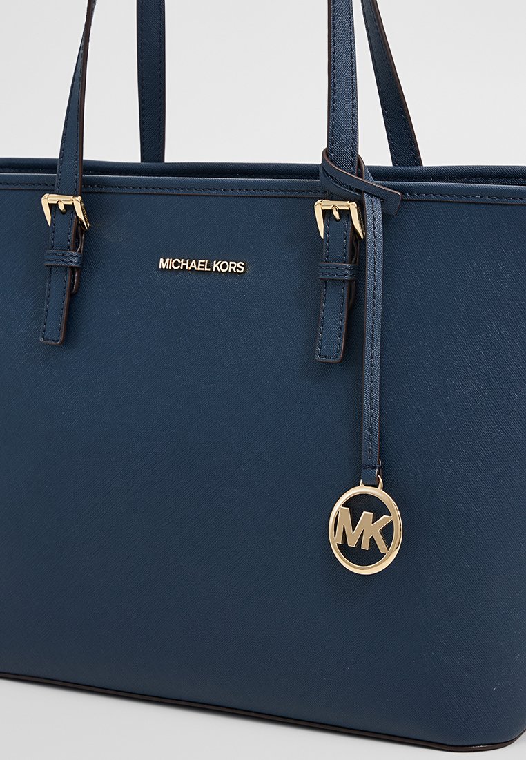 Sac fourre-tout synthétique bleu marine avec quincaillerie dorée et logo. Dispose de doubles poignées et d'une surface lisse et texturée. Design spacieux et rectangulaire.