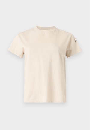 Femme portant un t-shirt beige et une longue jupe en jean bicolore, tenant un sac à main vert olive sur son épaule.