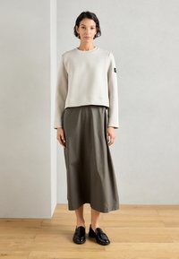 Sudadera corta gris claro de manga larga, combinada con una falda larga de color verde oliva. Los mocasines negros completan el atuendo.