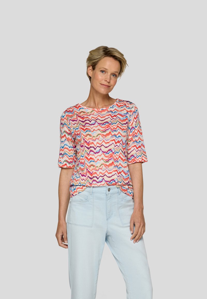 Short-sleeve T-shirt in a multicolored zigzag pattern featuring red, pink, blue, and cream hues. Fabric appears lightweight and soft.