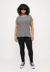 Sort og hvid stribet t-shirt med korte ærmer, parret med sorte skinny jeans og sorte og hvide sneakers. Model iført solbriller.