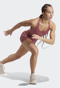 Sportstøj i lys pink; tætsiddende tanktop og shorts med glat tekstur. Sportssko i lys beige med snørebånd, der viser bevægelse.