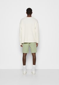 Maglietta oversize crema a maniche lunghe abbinata a pantaloni corti verde chiaro, con una vestibilità rilassata e texture a coste. Indossata con calze bianche e scarpe.