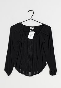 Blouse noire à manches longues avec un décolleté en U, en tissu texturé, avec un devant plissé et des détails en dentelle le long du centre et des poignets.
