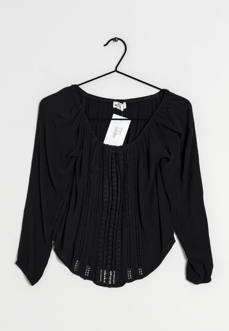 Blouse noire à manches longues avec un décolleté en U, en tissu texturé, avec un devant plissé et des détails en dentelle le long du centre et des poignets.
