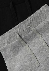 Grauer Baumwoll-Jogginghose mit schwarzem Stoff oben; mit passenden grauen Zugbändern und geripptem Material an den Kanten.