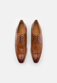 Scarpe da vestir in pelle marrone con design a punta d'ala, caratterizzate da dettagli perforati, punta rotonda e accenti scuri a contrasto sulla punta.