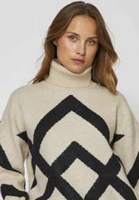 Bež pulover z black geometrijskim vzorcem, z visokim ovratnikom in oversize krojem, narejen iz strukturirane pletenine.