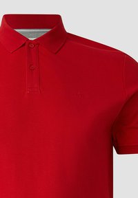 Polo rouge à manches courtes avec deux boutons sur le devant et un col plat, présentant une texture subtile et un petit logo brodé sur la poitrine.