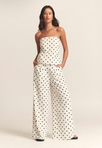White strapless top and wide-leg pants with black polka dots. The fabric appears lightweight and flowy, featuring pockets and a relaxed fit.