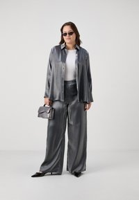 Gray satin-like blouse with pearl buttons, paired with wide-leg gray trousers. Accessories include a gray handbag and dark sunglasses.