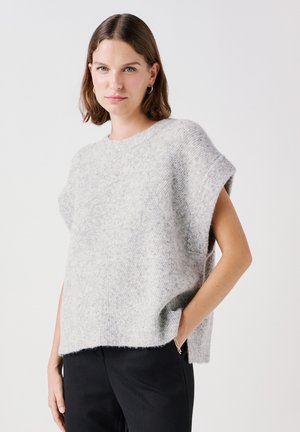 Pull en tricot gris à manches courtes, texture douce, encolure ronde et coupe décontractée. Porté sur un pantalon noir, dans une pose décontractée.