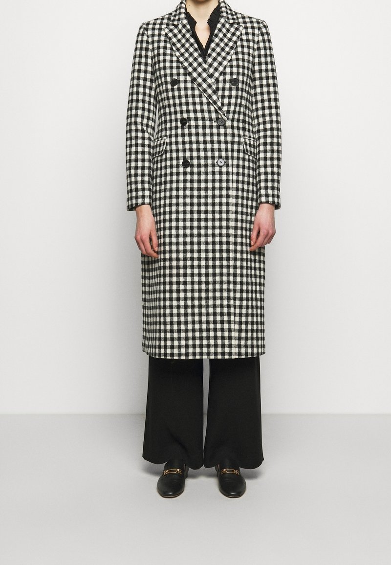 Double-breasted jas in zwart-witte ruitpatroon, gemaakt van gestructureerde stof, met reverskraag en twee knopen aan de voorkant.