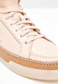 Baskets en cuir rose clair avec des accents beige contrastants, des lacets ronds et des coutures détaillées le long des bords. Texture lisse, design profil bas.