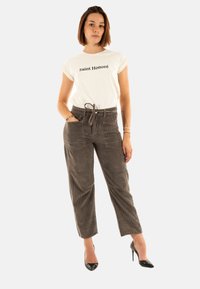 Maglietta bianca con "Saint Honoré" in testo nero, abbinata a pantaloni in velluto a coste marroni con vita regolabile e numerose tasche.
