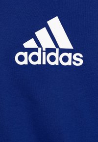 Blaues Baumwoll-Sweatshirt mit einem auffälligen weißen Adidas-Logo und drei diagonalen Streifen. Glatte Textur mit klassischem Rundhalsausschnitt.