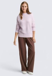 Svetlo vijoličen pleten pulover z okroglim ovratnikom, združen z rjavimi hlačami z visokim pasom in širokimi nogavicami ter belimi supergami.